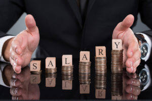 Midsection of businessman protecting Salary blocks on stacked coins at desk