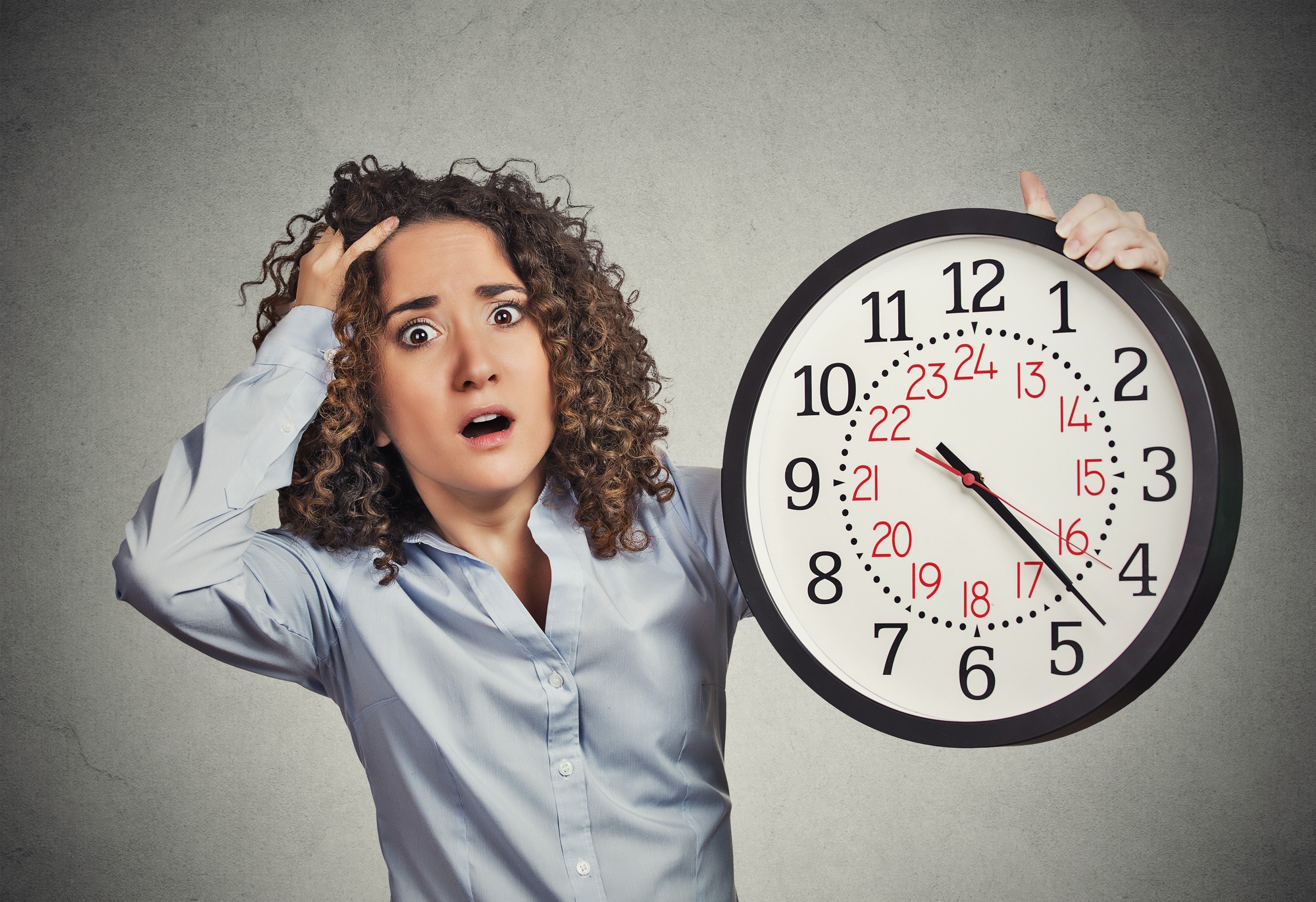 Time pressure. Closeup portrait woman stressed corporate employee holding clock looking anxiously running out of time isolated grey wall background. Human face expression emotion reaction. Last moment