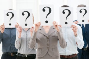 Business team hiding their faces behind question mark signs at office